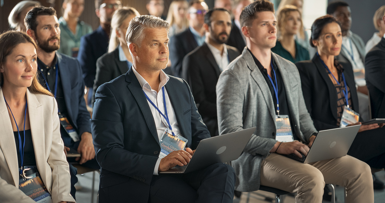 Aufmerksame Teilnehmende in der ersten Reihe des Publikums einer Konferenz